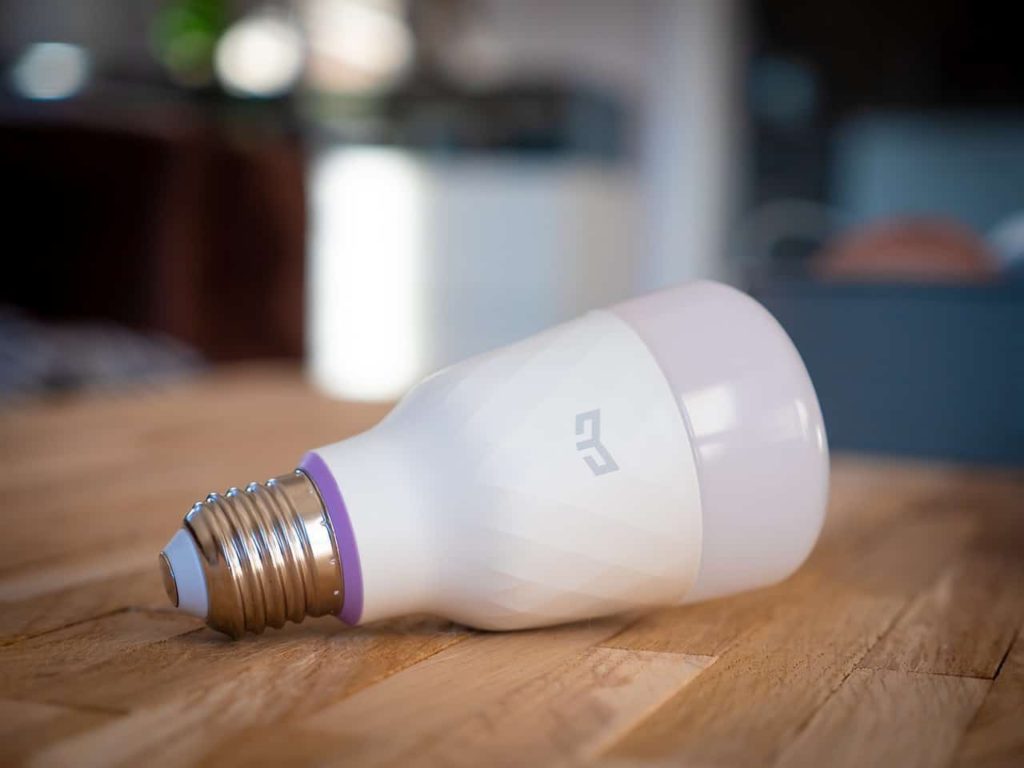 A smart bulb lying on a brown wooden kitchen table inside of a home.