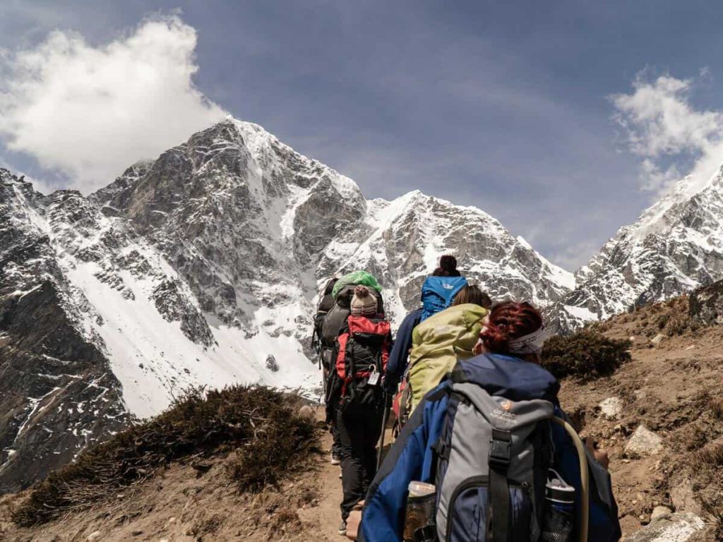 A group of five travelers in thick jackets hike up a mountain in a cold climate.